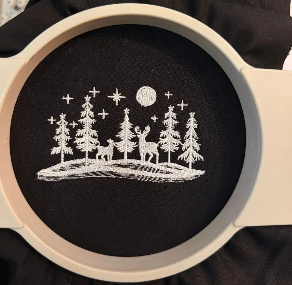 White winter forest and deer scene embroidered on black fabric